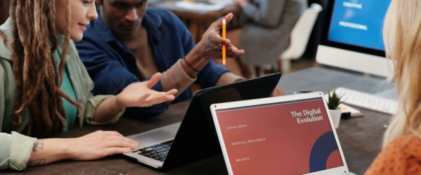 Diverse team collaborating with laptops in a modern office setting, discussing digital evolution.